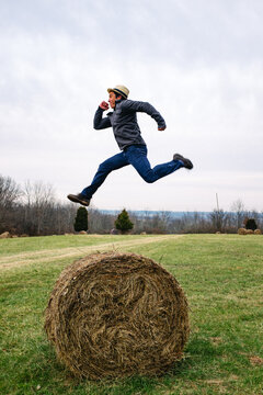 A man jumping high in the air over a round hay bail in a field
