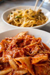 Noodles with mushrooms and vegetables and kimchi in white bowl close-up on gray background
