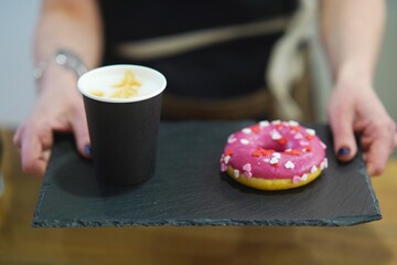 Barista holds out a tray with a donut and coffee. Donut and coffee tray