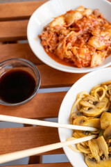 Noodles with mushrooms and vegetables and kimchi in white bowl close-up on gray background	
