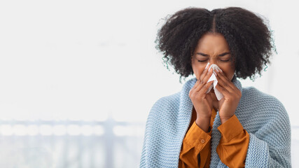 A young woman with curly hair appears unwell, blowing her nose with a tissue