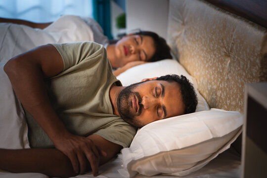 handheld shot of Indian Married Couples sleeping peacefully at night in comfortable on bed at bedroom - concept of relaxation, togetherness and wellbeing