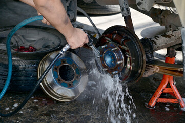 Closeup of Maintenance technician Using a hose to spray water on the brake disc assembly of a...