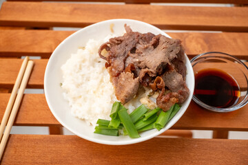 Asian style local beef steak in white rice served with chopsticks and soy sauce in a white bowl on the restaurant table
