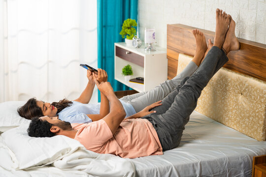 Happy Romantic relaxed couples using mobile phone by laying on bed - concept of affection, intimacy and social media sharing