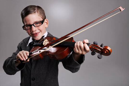 Smile, music and child with violin in studio for practice with suit and glasses for fashion. Happy, style and portrait of young boy kid play string instrument with spectacles by gray background.