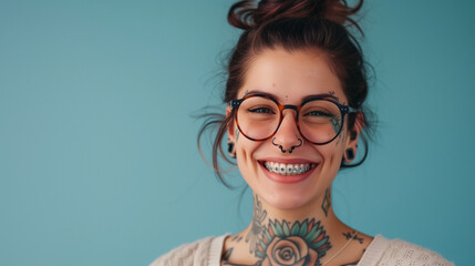 A joyful woman with glasses, a vibrant smile showing braces, and tattoos, exuding confidence and individuality. - obrazy, fototapety, plakaty