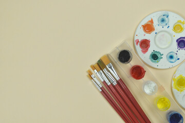 Top view of art palette, watercolor and a brush on orange background and copy space.