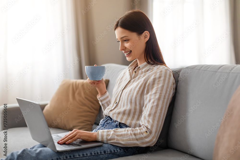 Wall mural relaxed young woman with coffee and laptop on couch