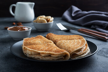 Pancakes with chocolate banana filling. Delicious breakfast of pancakes envelopes on a plate, dark concrete background.