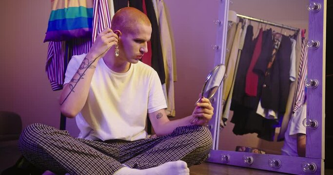 LGBT Individual Trying on Earrings by Large Mirror in Dressing Room