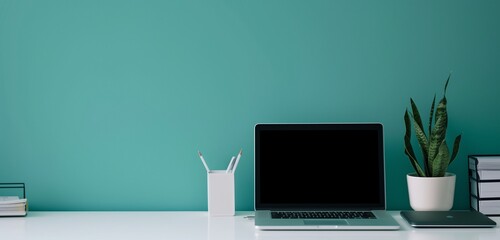 Sleek laptop, documents, pencil holder on white table; vibrant teal background in a modern office.
