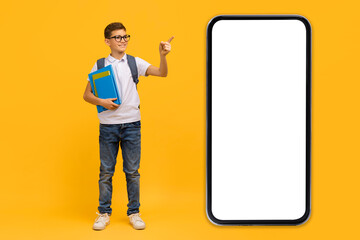 Educational App. Excited Teen Schoolboy Pointing At Smartphone With Blank Black Screen