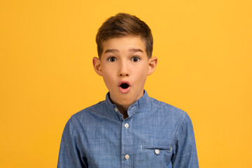 Astonished teenage boy with wide-eyed expression posing against yellow studio background