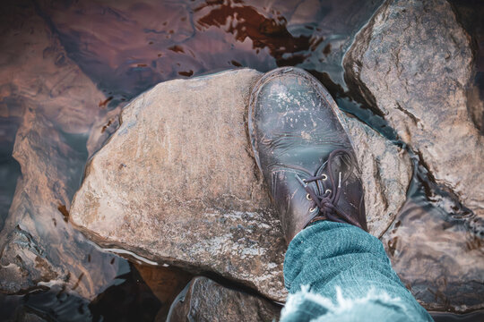 Muddy leather shoe stepping on a stone in the water, walking and hiking adventure in the countryside