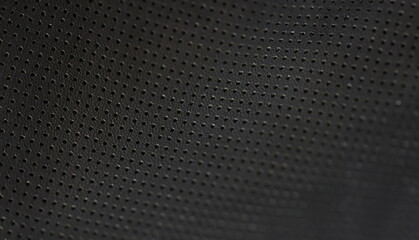 Black leather fabric pattern of small holes, close-up. Perforated matte texture. A macro shot of...