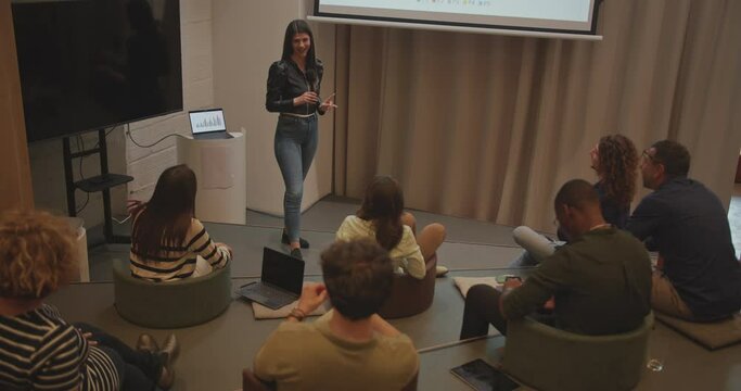 In an amphitheater room during a business seminar, a high view captures a group of international and multiage people engaging in discussions and interactions. The scene embodies the concept of work