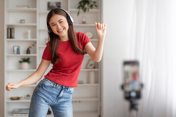 Young asian woman wearing headphones dancing and recording video at home
