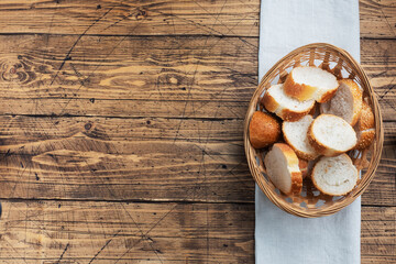 Fresh white bread, baguette slices in a wicker basket. Wooden rustic table background. Copy space