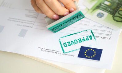 A hand puts a stamp approved on a document for a visa to Europe, close-up. Preparation of documents...