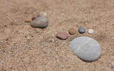 Fototapeta na wymiar Footprint of stones in the sand, close-up. Wallpaper concept vacation at sea, borders open, beach season
