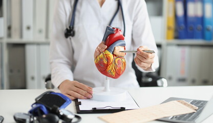 Woman doctor shows a plastic model of the heart, close-up. Training material for a cardiologist, a surgeon's workplace