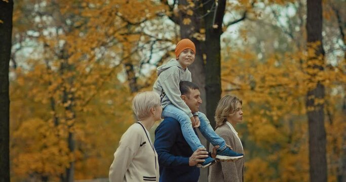 happy boy sitting on father shoulders during family walk in park in autumn day, 4K, Prores