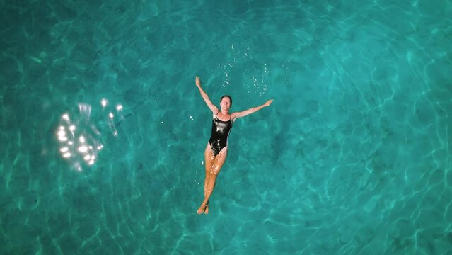 Serene swim in turquoise waters. A person floating peacefully in clear sea, aerial top down view of woman floating in ocean.