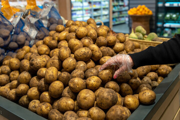 The hand takes a potato close-up. Buying potatoes and vegetables at the grocery store.