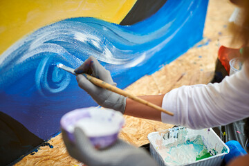 Female artist hand applies small brushstrokes of paint with paintbrush to canvas creating picture for exhibition, close up view of female hand painter creative process