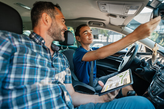 Driving instructor sitting in a car with his student and explain to him driving basics and traffic rules. He is using electronic tablet for education purpose. View from inside.
