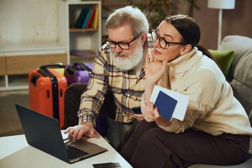 Senior man and woman sitting at home and using laptop for booking, planning trip, buying tickets...