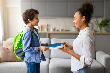 Black mother giving school supplies to excited son