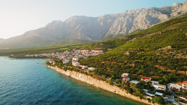 Cliffside town at dusk. Human settlement that hugs the Adriatic coastline. Makarska Riviera with the rough Biokovo mountains by sea.