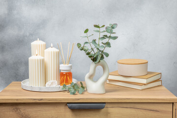 Green eucalyptus leaves in a vase stand on a chest of drawers against the background of a wall. Aromatherapy.Beautiful eucalyptus bouquet.Minimalist interior with flowers, candles and aroma diffuser.