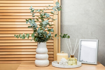 Green eucalyptus leaves in a vase stand on a chest of drawers against the background of a wall. Aromatherapy.Beautiful eucalyptus bouquet.Minimalist interior with flowers, candles and aroma diffuser.