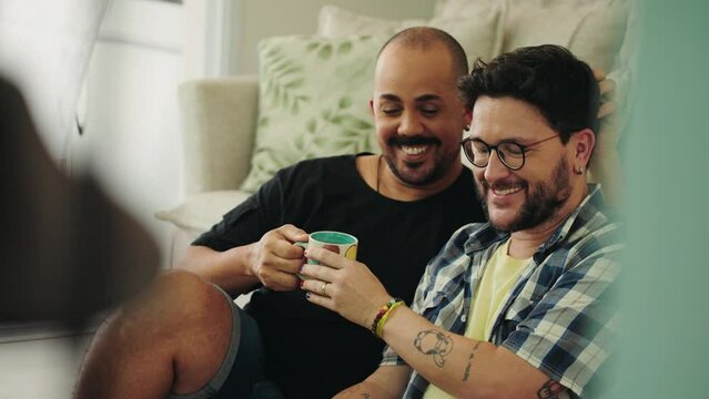 Hispanic male gay couple spend free time using laptop, enjoy leisure on internet, buy goods, discuss e-services purchase, planning vacation, buy tickets.
