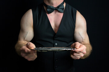 Muscular Waiter in Black Vest and Bare Arms Holding Serving Tray. Sexy Bodybuilding Butler.
