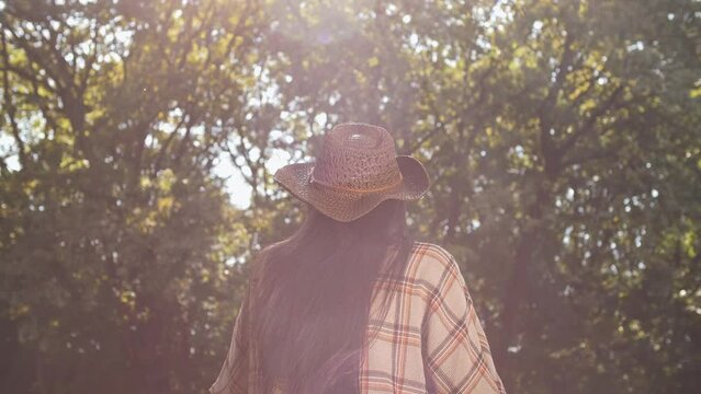 Dreamy brunet with long straight hair wearing a plaid shirt and a wicker hat in the woods in the sunshine 