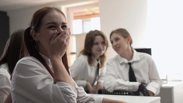 Young schoolgirl friends gossip in class and then joke and laugh loudly together 