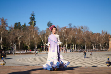 a little girl dancing flamenco dressed in a beige dress with ruffles and purple fringes in a famous...