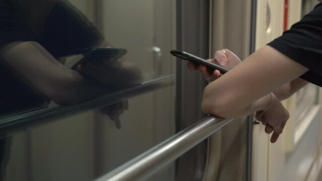 Closeup in the hands of a smartphone of a modern woman who stands in the corridor of a compartment car of a moving train, leaning on the handrail, the girl uses her gadget