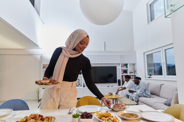A young Arab woman gracefully prepares iftar for her family, delicately serving the table in the...