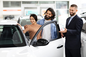 Young indian loving couple choosing car at luxury auto dealership