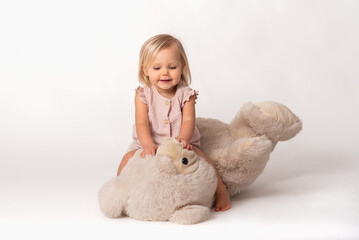 happily smiling little girl sitting on a big teddy bear