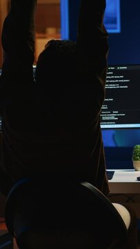 Man doing IT support job from home office, stretching after sitting on desk chair all day. Programmer loosening up, relaxing after typing on computer for long period of time, camera A
