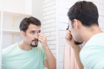 Handsome man grooming in front of the mirror in the bathroom. Young guy depilates with tweezers 