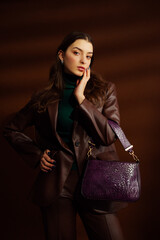 Fashionable confident woman wearing faux leather suit blazer, pants, green turtleneck, holding...