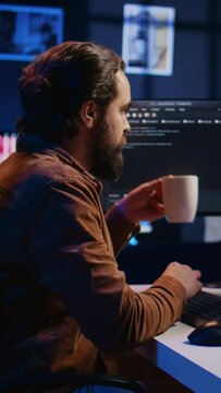 Computer scientist drinking cup of coffee while developing code on PC using java programming languages. IT admin brainstorming ways of fixing database errors, enjoying hot beverage, camera B