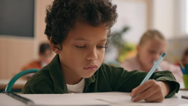 Smart African American guy boy think writing notes task exercise class lesson school learn write in copybook kid schoolboy son child pupil thinking learning studying primary education at table desk
